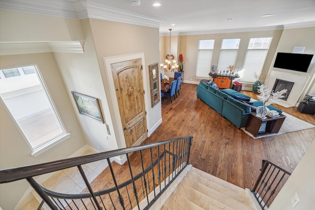 stairs with a notable chandelier, plenty of natural light, a fireplace, and ornamental molding