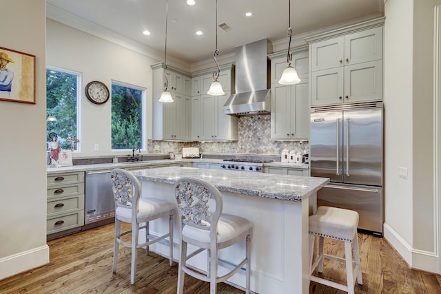 kitchen featuring light stone countertops, a center island, wall chimney exhaust hood, pendant lighting, and appliances with stainless steel finishes