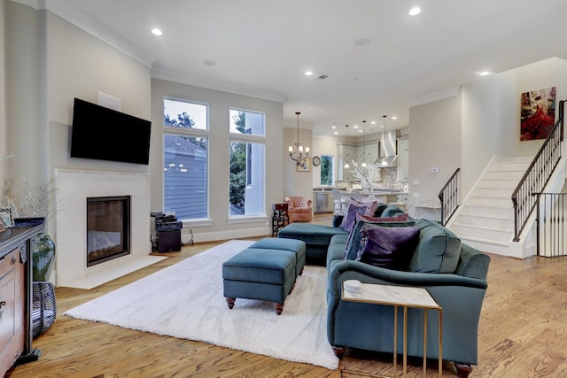 living room featuring crown molding, a high end fireplace, light hardwood / wood-style floors, and an inviting chandelier