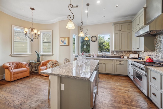 kitchen featuring a kitchen breakfast bar, stainless steel stove, hanging light fixtures, and wall chimney range hood