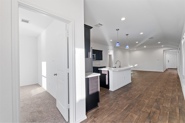 kitchen featuring hanging light fixtures, dark wood-type flooring, and a center island with sink