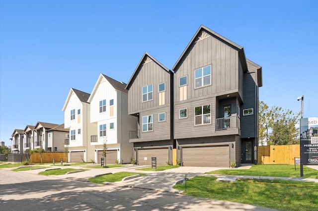 multi unit property featuring an attached garage, fence, concrete driveway, a residential view, and board and batten siding