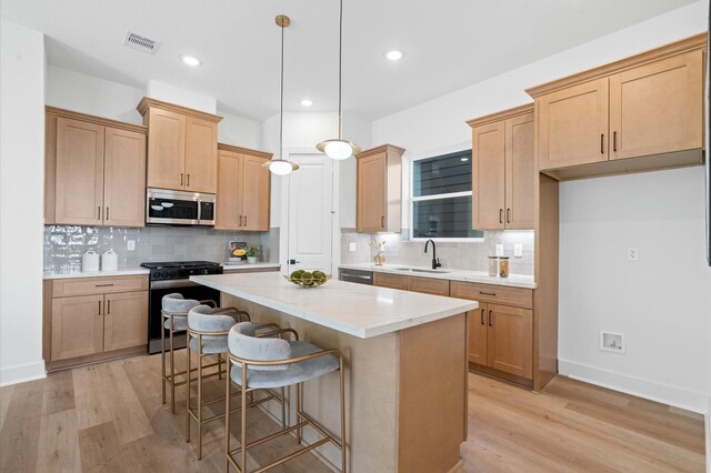 kitchen with sink, hanging light fixtures, light wood-type flooring, a kitchen island, and stainless steel appliances