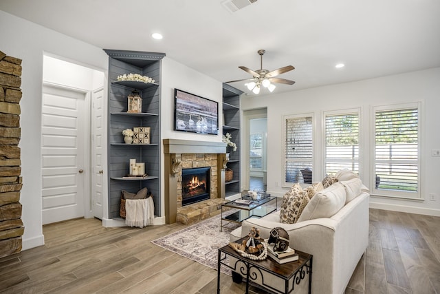 living room featuring hardwood / wood-style floors, ceiling fan, and a stone fireplace
