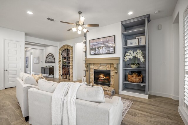 living room with ceiling fan, a stone fireplace, and wood-type flooring