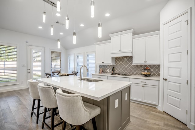 kitchen with sink, an island with sink, pendant lighting, and white cabinets