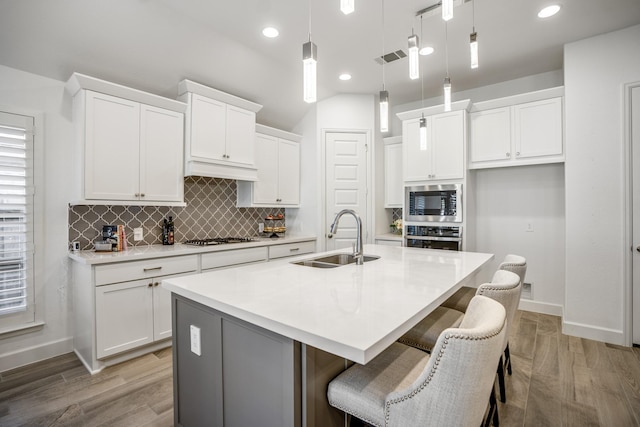 kitchen with appliances with stainless steel finishes, hanging light fixtures, an island with sink, sink, and white cabinetry