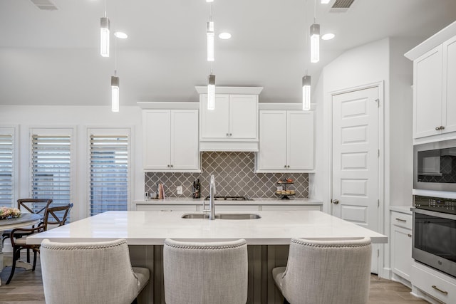 kitchen with white cabinetry, a kitchen island with sink, hanging light fixtures, and stainless steel oven