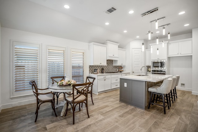 kitchen featuring appliances with stainless steel finishes, sink, white cabinets, hanging light fixtures, and a kitchen island with sink