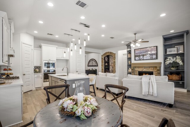 dining space with sink, ceiling fan, a stone fireplace, and light hardwood / wood-style flooring