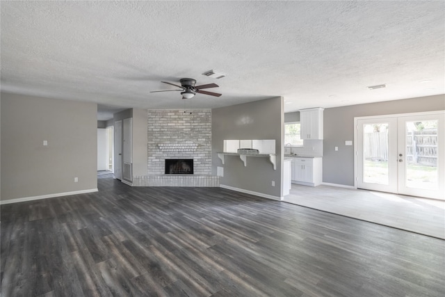 unfurnished living room featuring dark hardwood / wood-style floors, ceiling fan, a brick fireplace, a textured ceiling, and french doors