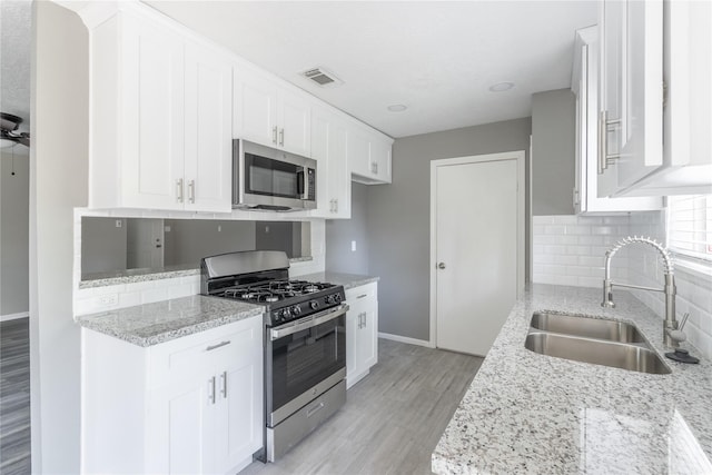 kitchen featuring appliances with stainless steel finishes, sink, white cabinets, and light stone counters