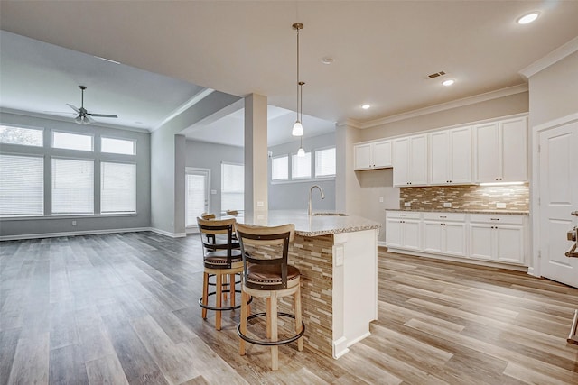 kitchen featuring a breakfast bar, hanging light fixtures, an island with sink, tasteful backsplash, and white cabinetry