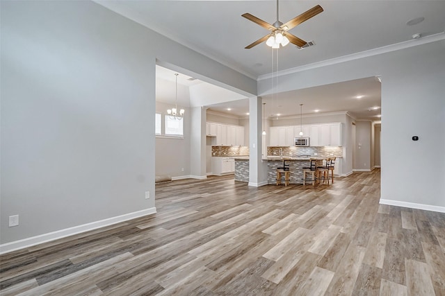 unfurnished living room featuring ceiling fan with notable chandelier, light hardwood / wood-style floors, and ornamental molding