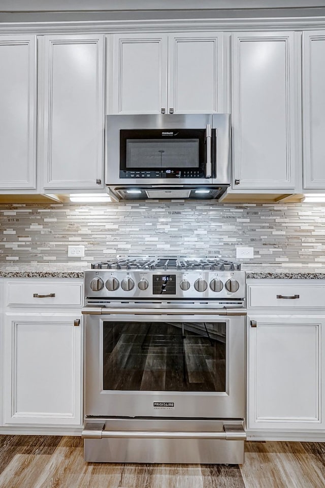 kitchen with light stone countertops, appliances with stainless steel finishes, backsplash, light hardwood / wood-style flooring, and white cabinetry