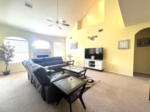 carpeted living room featuring a tiled fireplace, ceiling fan, and high vaulted ceiling