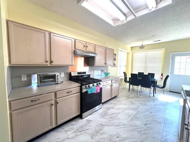 kitchen featuring gas range, light brown cabinetry, a healthy amount of sunlight, and a textured ceiling