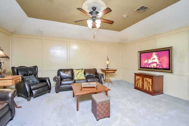 living room with a raised ceiling, ceiling fan, and light colored carpet