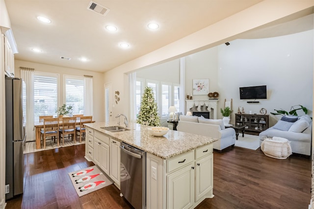 kitchen with sink, dark wood-type flooring, stainless steel appliances, light stone counters, and an island with sink