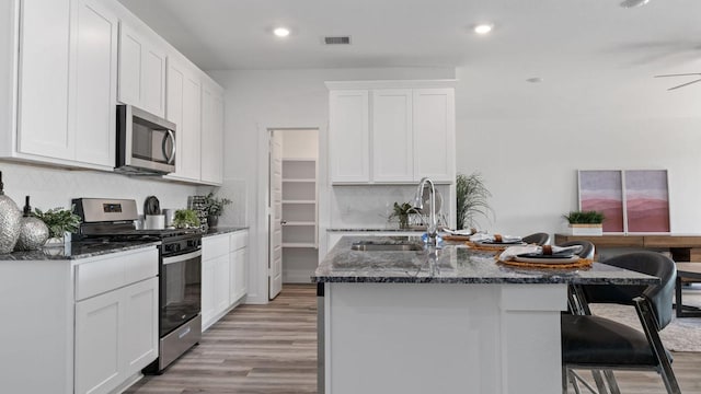 kitchen with white cabinets, sink, a breakfast bar area, dark stone countertops, and stainless steel appliances