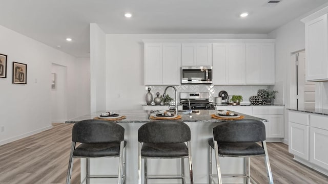 kitchen featuring dark stone countertops, white cabinets, an island with sink, and stainless steel appliances