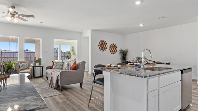 kitchen with a kitchen island with sink, white cabinets, sink, dark stone countertops, and light wood-type flooring