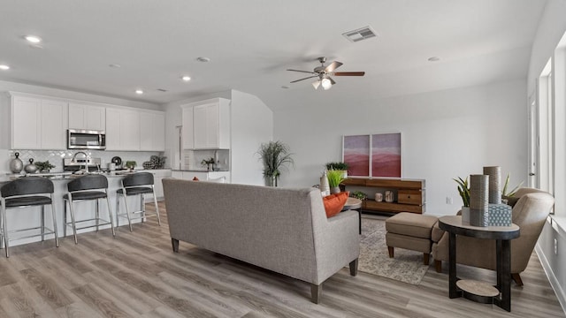 living room with light wood-type flooring, ceiling fan, and sink