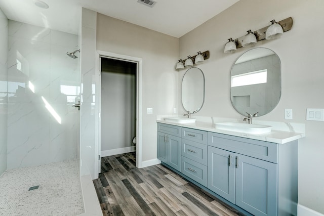 bathroom featuring a tile shower, vanity, wood-type flooring, and toilet