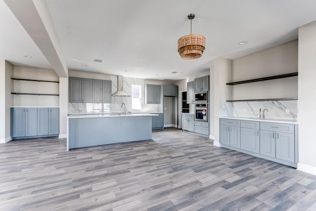 kitchen featuring backsplash, stainless steel appliances, gray cabinets, and wall chimney exhaust hood