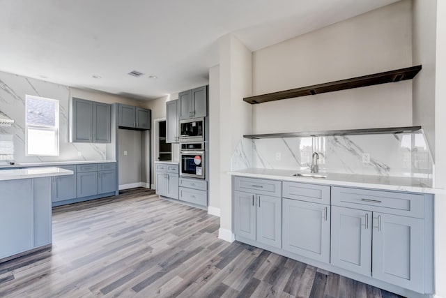 kitchen with backsplash, sink, light hardwood / wood-style floors, and appliances with stainless steel finishes