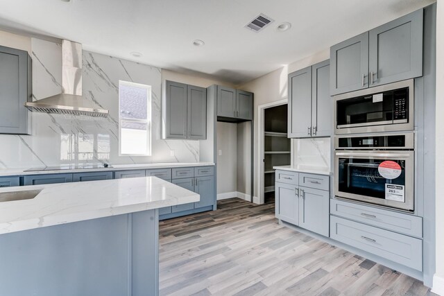 kitchen with decorative backsplash, light stone countertops, wall chimney exhaust hood, and appliances with stainless steel finishes