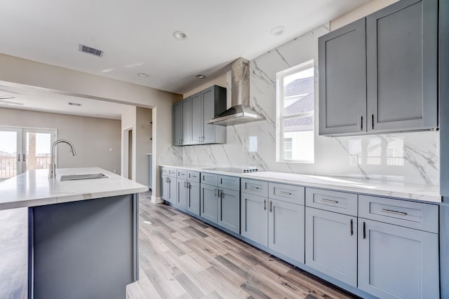 kitchen featuring a kitchen island with sink, wall chimney range hood, sink, decorative backsplash, and black electric cooktop