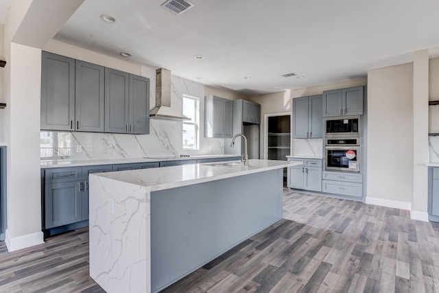 kitchen with sink, a center island with sink, wall chimney exhaust hood, and appliances with stainless steel finishes