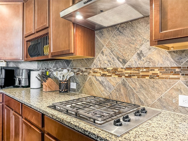 kitchen featuring decorative backsplash, light stone countertops, stainless steel gas stovetop, and wall chimney range hood