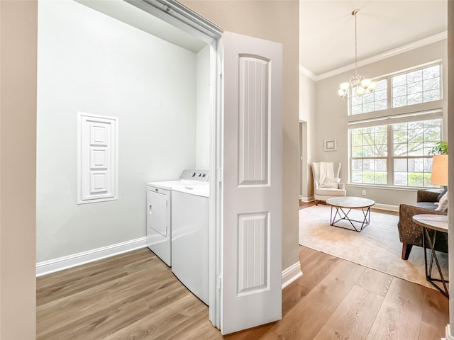 clothes washing area featuring washing machine and dryer, ornamental molding, light hardwood / wood-style flooring, and an inviting chandelier