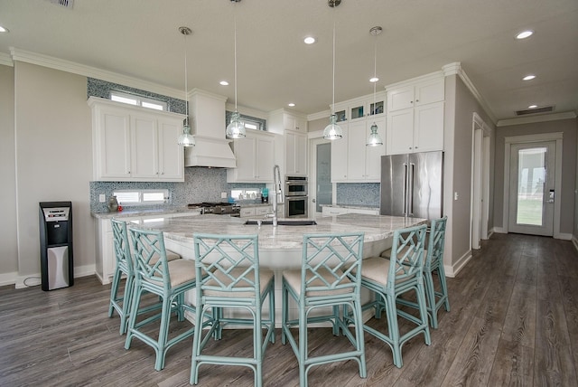 kitchen featuring white cabinets, a large island with sink, decorative light fixtures, and stainless steel appliances