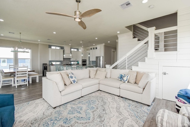 living room with ceiling fan with notable chandelier, wood-type flooring, and crown molding