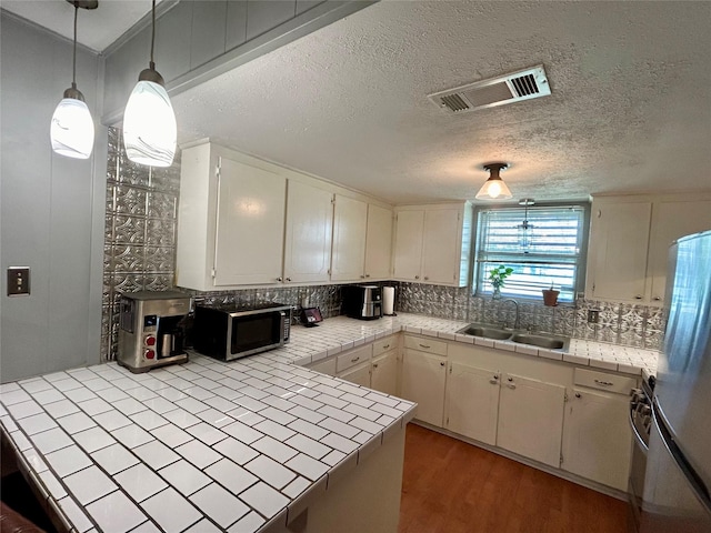 kitchen featuring hanging light fixtures, stainless steel refrigerator, tile counters, and sink