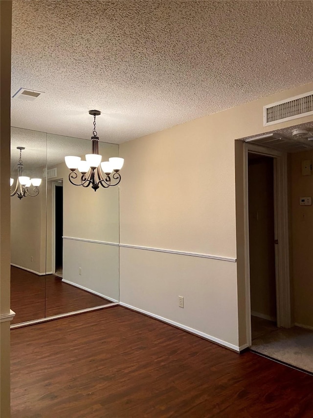 unfurnished room with a notable chandelier, dark hardwood / wood-style floors, and a textured ceiling