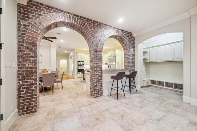 kitchen featuring double oven, crown molding, ceiling fan, and brick wall