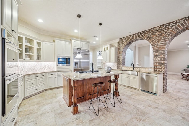 kitchen with a center island, sink, hanging light fixtures, light stone counters, and built in appliances