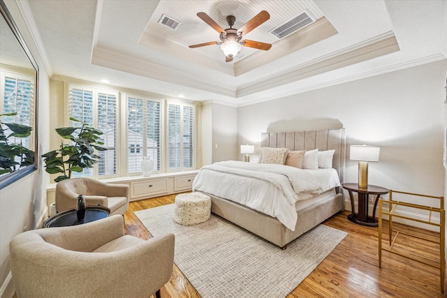 bedroom with light wood-type flooring, a raised ceiling, ceiling fan, and ornamental molding