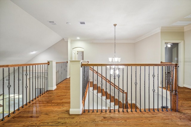 corridor featuring wood-type flooring, ornamental molding, and a chandelier