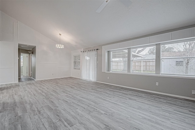 unfurnished living room featuring lofted ceiling, ceiling fan with notable chandelier, light hardwood / wood-style flooring, and a textured ceiling