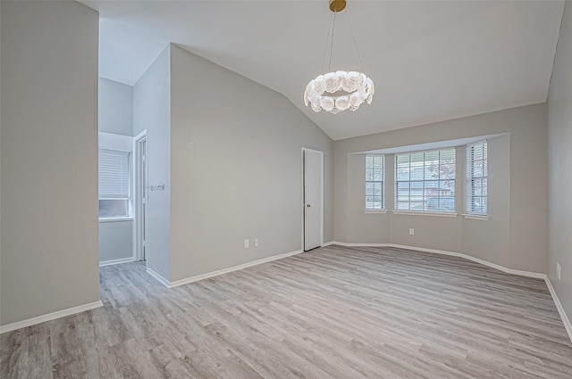 spare room with a notable chandelier, vaulted ceiling, and light wood-type flooring