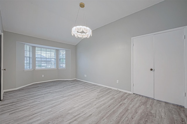 unfurnished room featuring vaulted ceiling, an inviting chandelier, and light hardwood / wood-style flooring