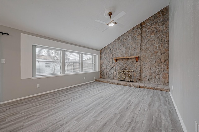 unfurnished living room featuring vaulted ceiling, ceiling fan, a fireplace, and light hardwood / wood-style floors