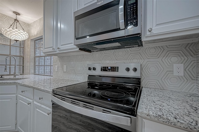 kitchen with sink, appliances with stainless steel finishes, white cabinetry, backsplash, and hanging light fixtures