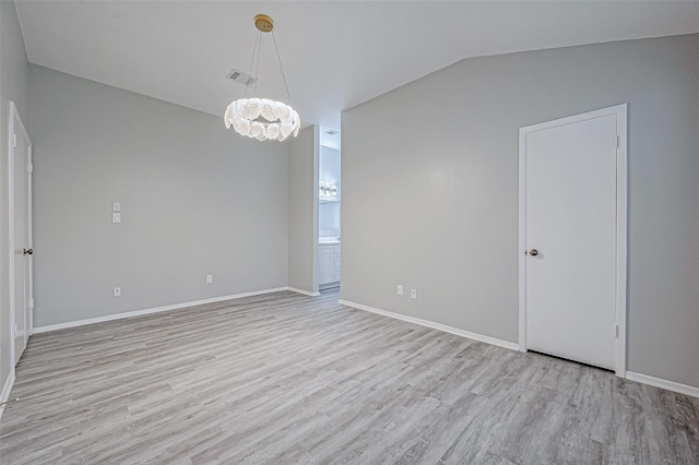 spare room featuring an inviting chandelier, vaulted ceiling, and light wood-type flooring