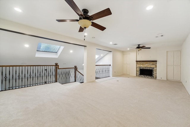 unfurnished living room with a stone fireplace, light carpet, ceiling fan, and a skylight